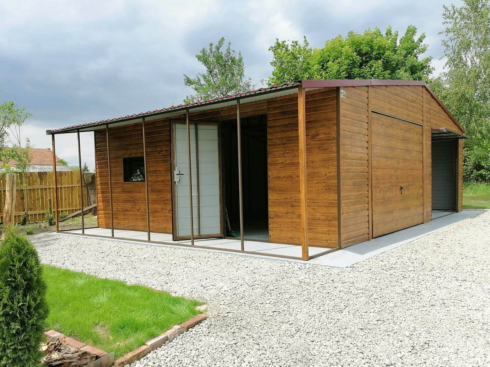 Garaż blaszany złoty dąb 8 x 6 + wiatka 1 x 6 dach dwuspadowy widok boczny jedna z bram zamknięta, druga podniesiona, drzwi boczne otwarte, okno uchylone