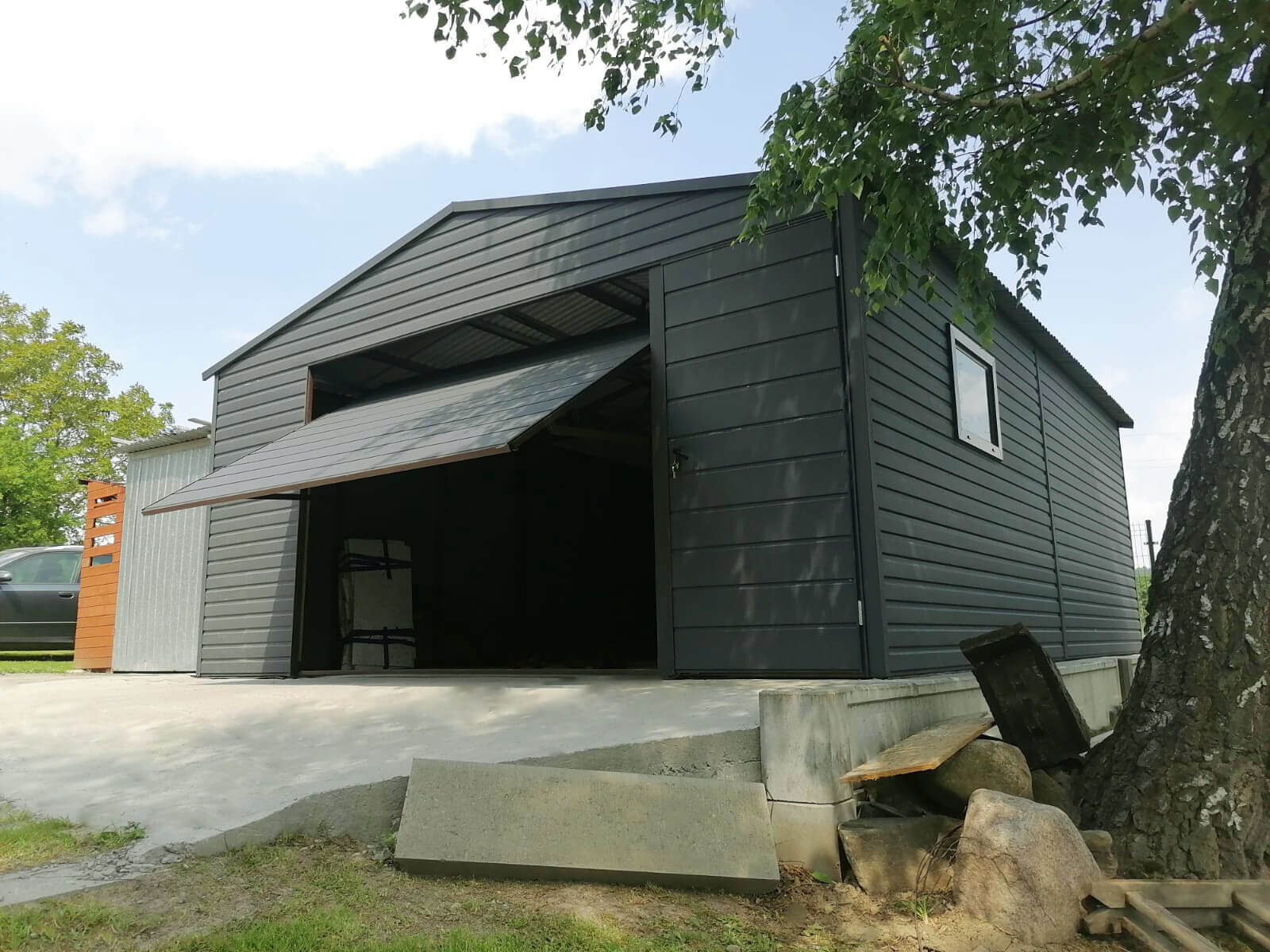 Garaż blaszany 5 x 6 Grafit Mat jednostanowiskowy, dwuspadowy, widok frontowy od dołu, brama uchylna podniesiona, drzwi frontowe zamknięte