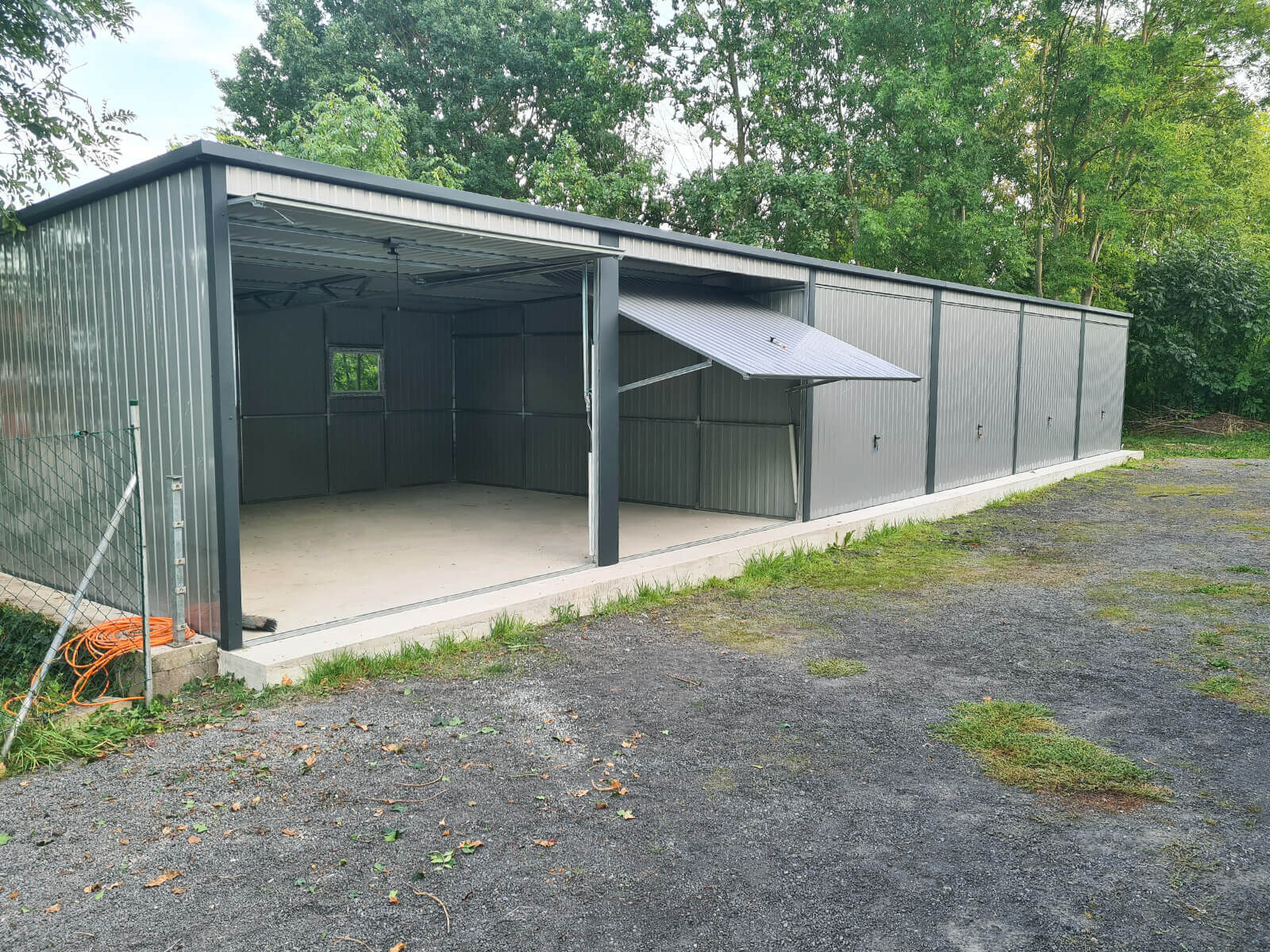 Garaż blaszany sześciostanowiskowy 18 x 5, spad dachu do tyłu widok z przodu, dwie z sześciu bram są podniesione do góry