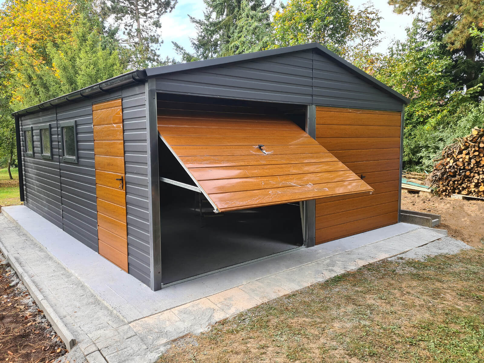 Garaż blaszany 6 x 7 Złoty dąb + Grafit Mat drzwi, 3 okna przód garażu z jedną podniesioną bramą, druga opuszczona